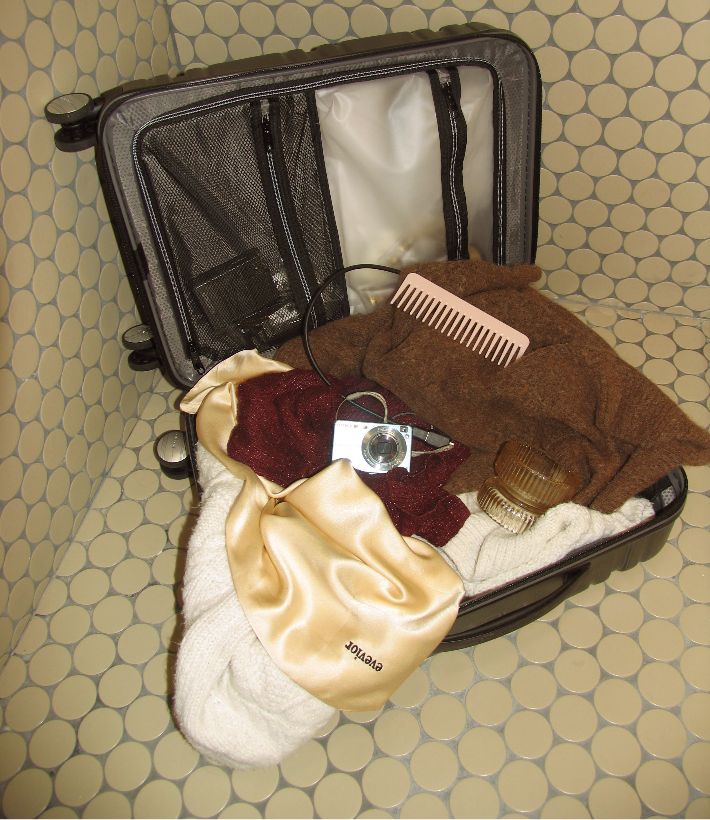 Open suitcase with a champagne silk pillowcase and travel essentials inside.
