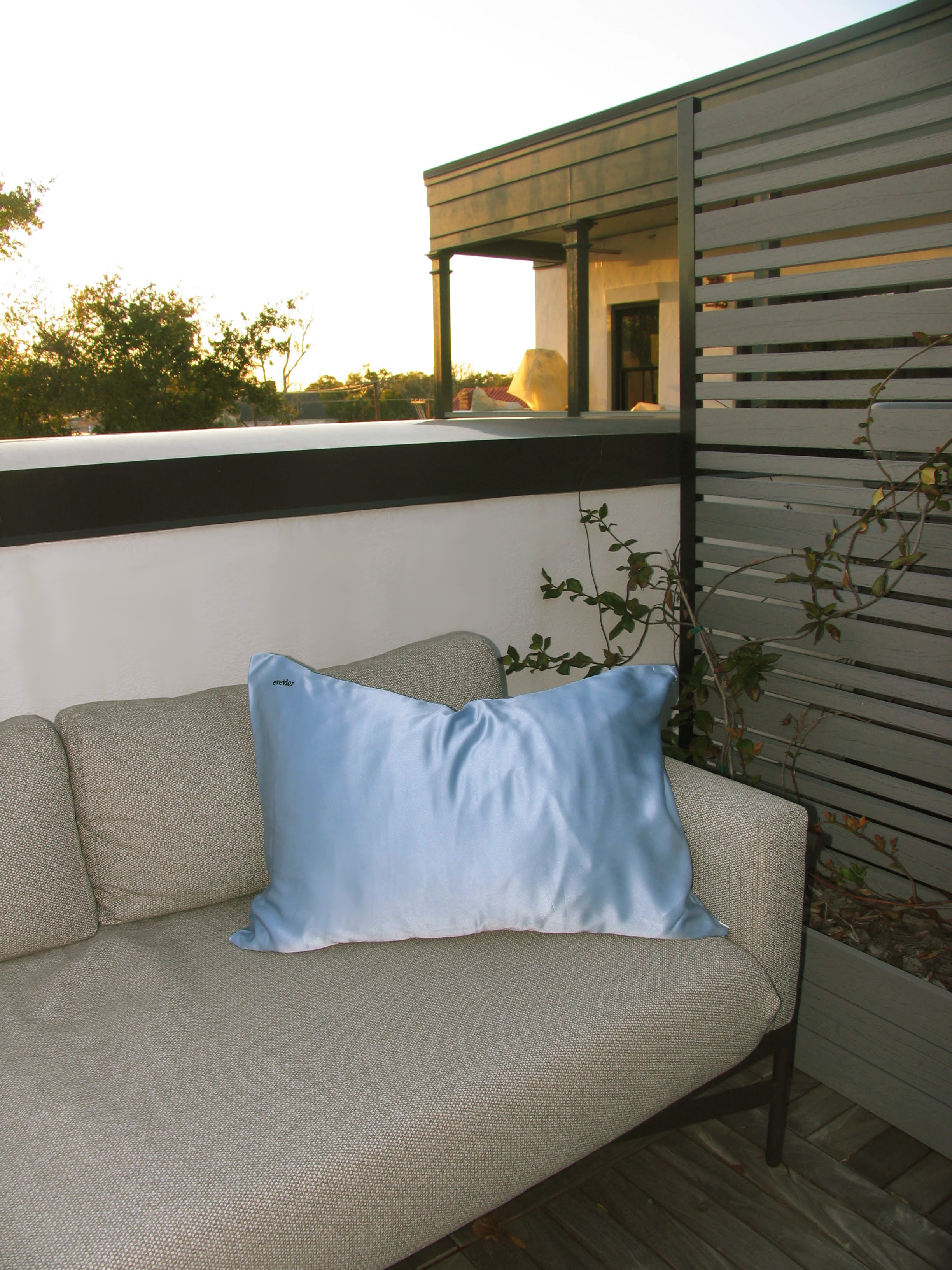 Blue silk pillowcase styled on an outdoor lounge chair at sunset.