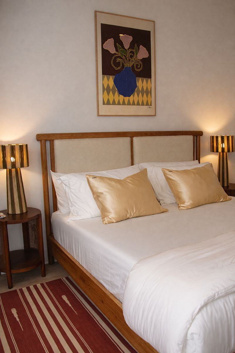 Wooden bed with white bedding and two champagne silk pillows.