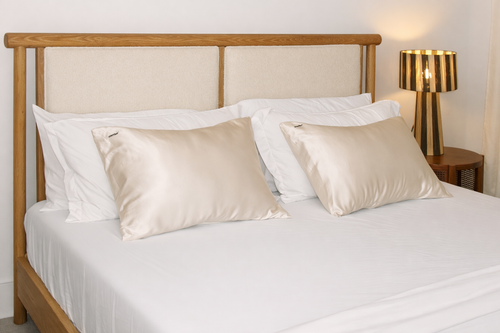 Two pearl white silk pillows on a neatly made white bed.