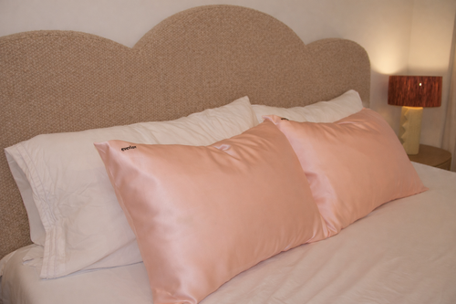 Two blush pink silk pillows on a neatly made bed.