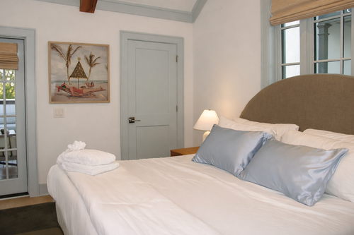 Neatly made bed with powder blue silk pillows in a bright bedroom.
