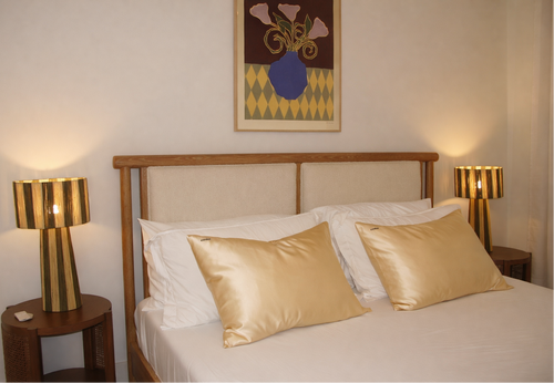 Neatly made bed with two champagne silk pillows and warm bedside lamps.