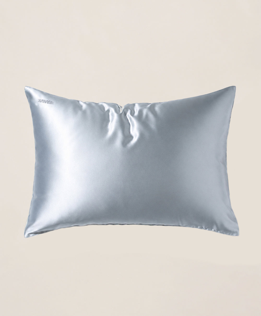 A pillow covered in a light blue silk pillowcase with a subtle sheen, shown against a solid beige background.