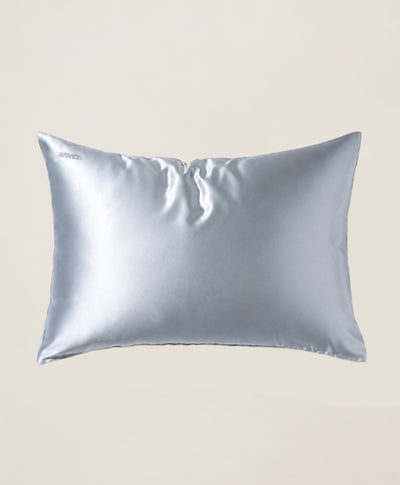 A pillow covered in a light blue silk pillowcase with a subtle sheen, shown against a solid beige background.