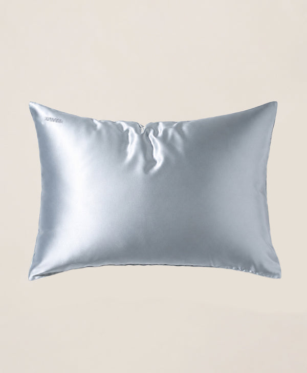 A pillow covered in a light blue silk pillowcase with a subtle sheen, shown against a solid beige background.