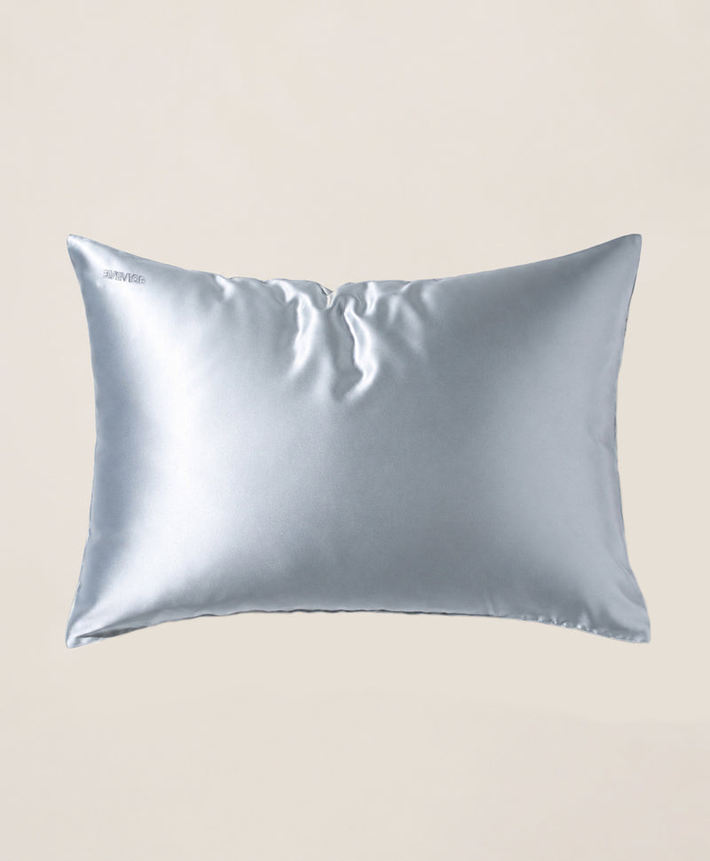 A pillow covered in a light blue silk pillowcase with a subtle sheen, shown against a solid beige background.