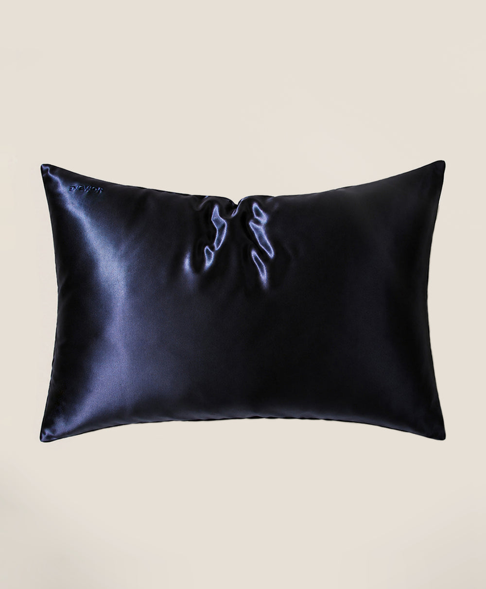 A pillow covered in a dark navy blue silk pillowcase with a subtle sheen, shown against a solid beige background