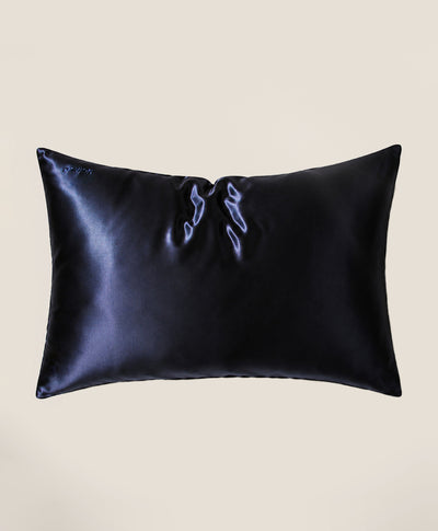 A pillow covered in a dark navy blue silk pillowcase with a subtle sheen, shown against a solid beige background