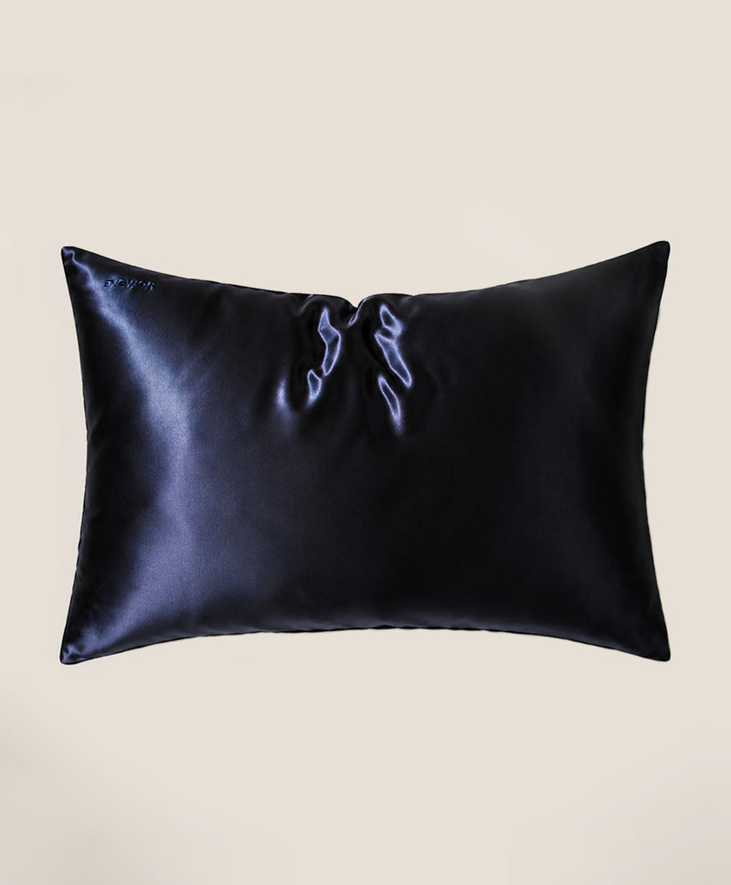 A pillow covered in a dark navy blue silk pillowcase with a subtle sheen, shown against a solid beige background