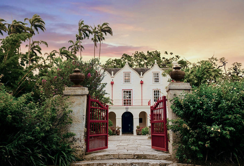 A white Jacobian-style mansion at dusk seen through its gate.