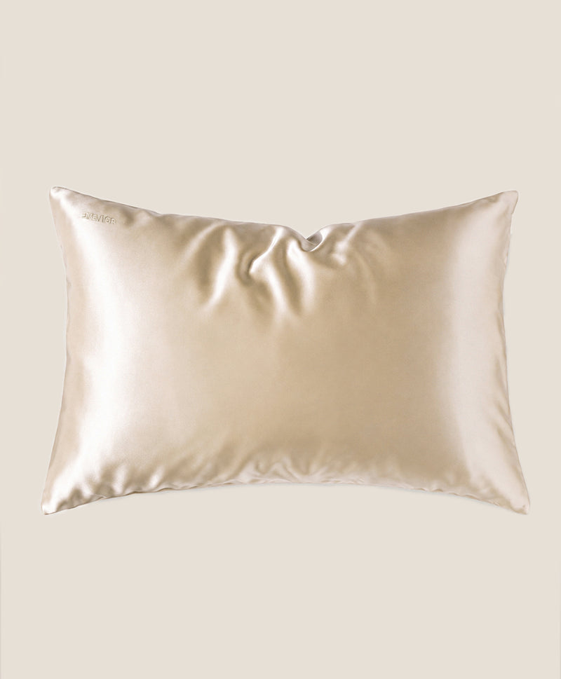 A pillow covered in a beige silk pillowcase with a subtle sheen, shown against a solid beige background