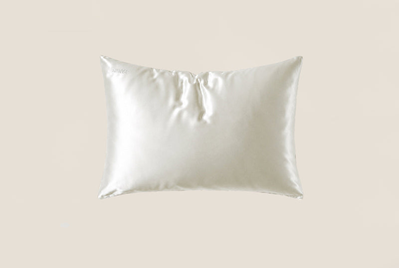 A white silk pillowcase with a gathered center top, shown against a solid beige background.