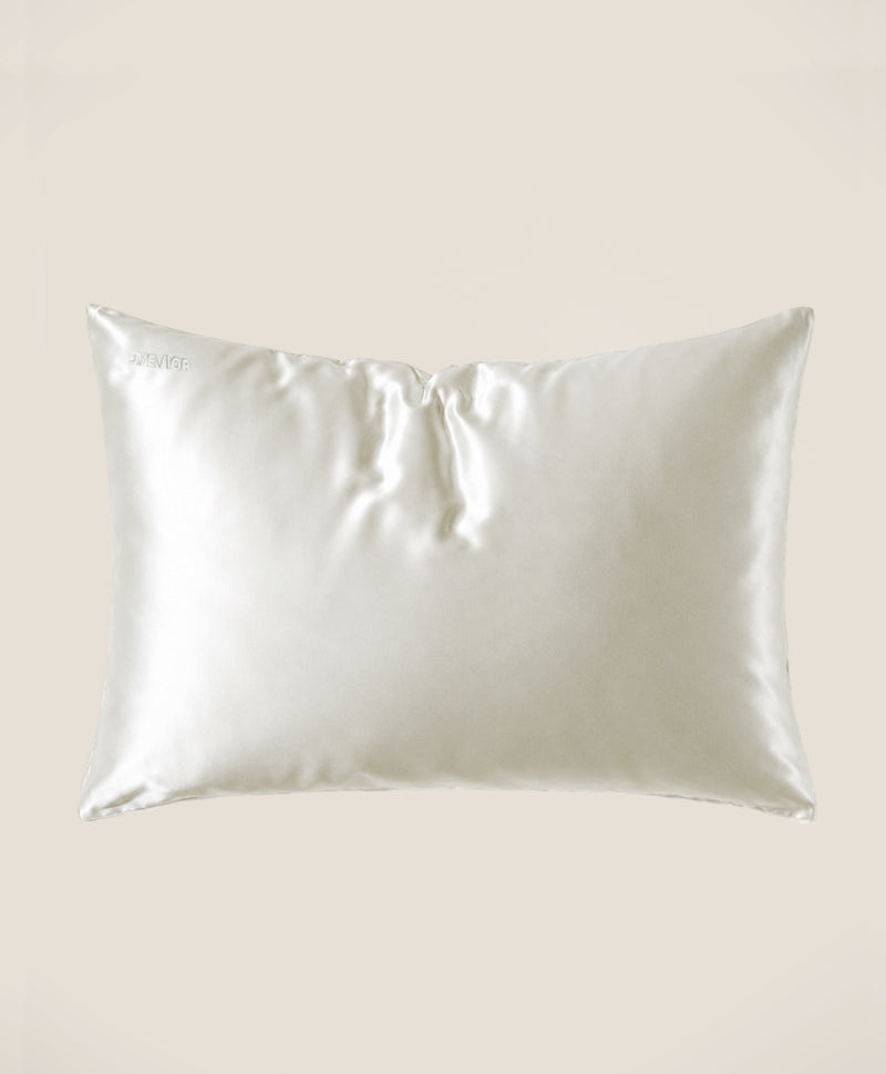 A pillow covered in a cream silk pillowcase with a subtle sheen, shown against a solid beige background
