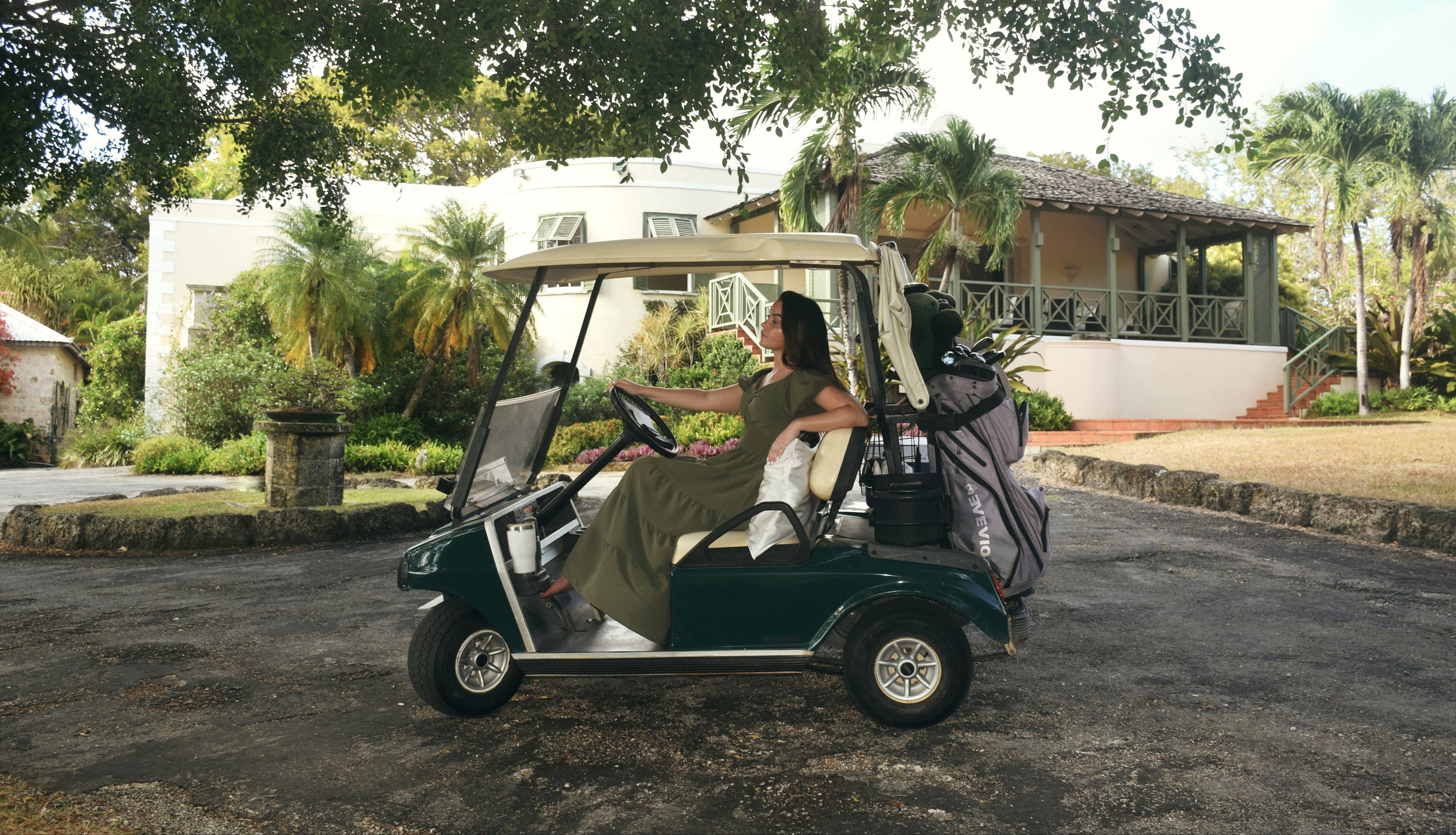 Woman in a green golf cart leaning on a white silk pillowcase on a paved road with a scenic background.