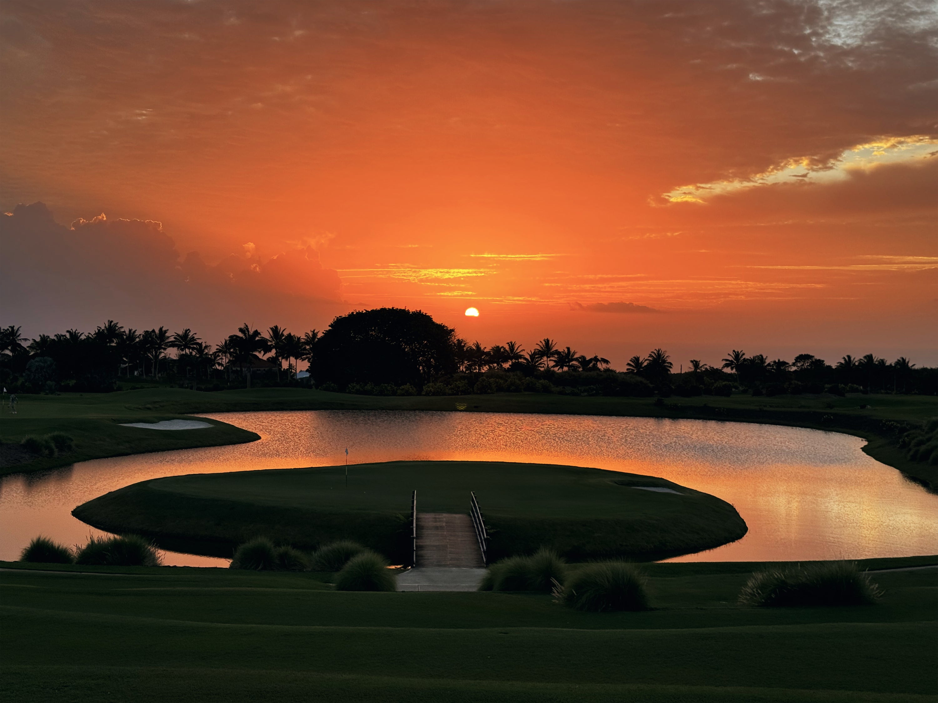 Golf course with a lake with an island in the middle and sunset sky.