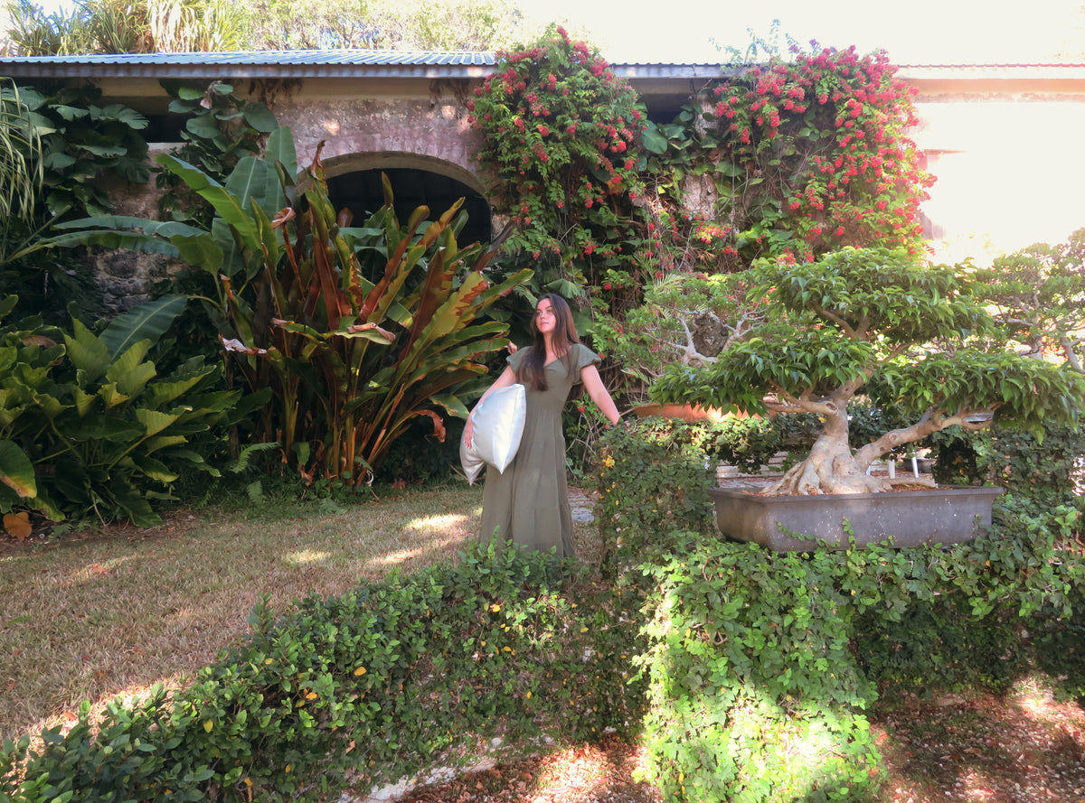 Woman holding white silk pillow in lush garden filled with greenery